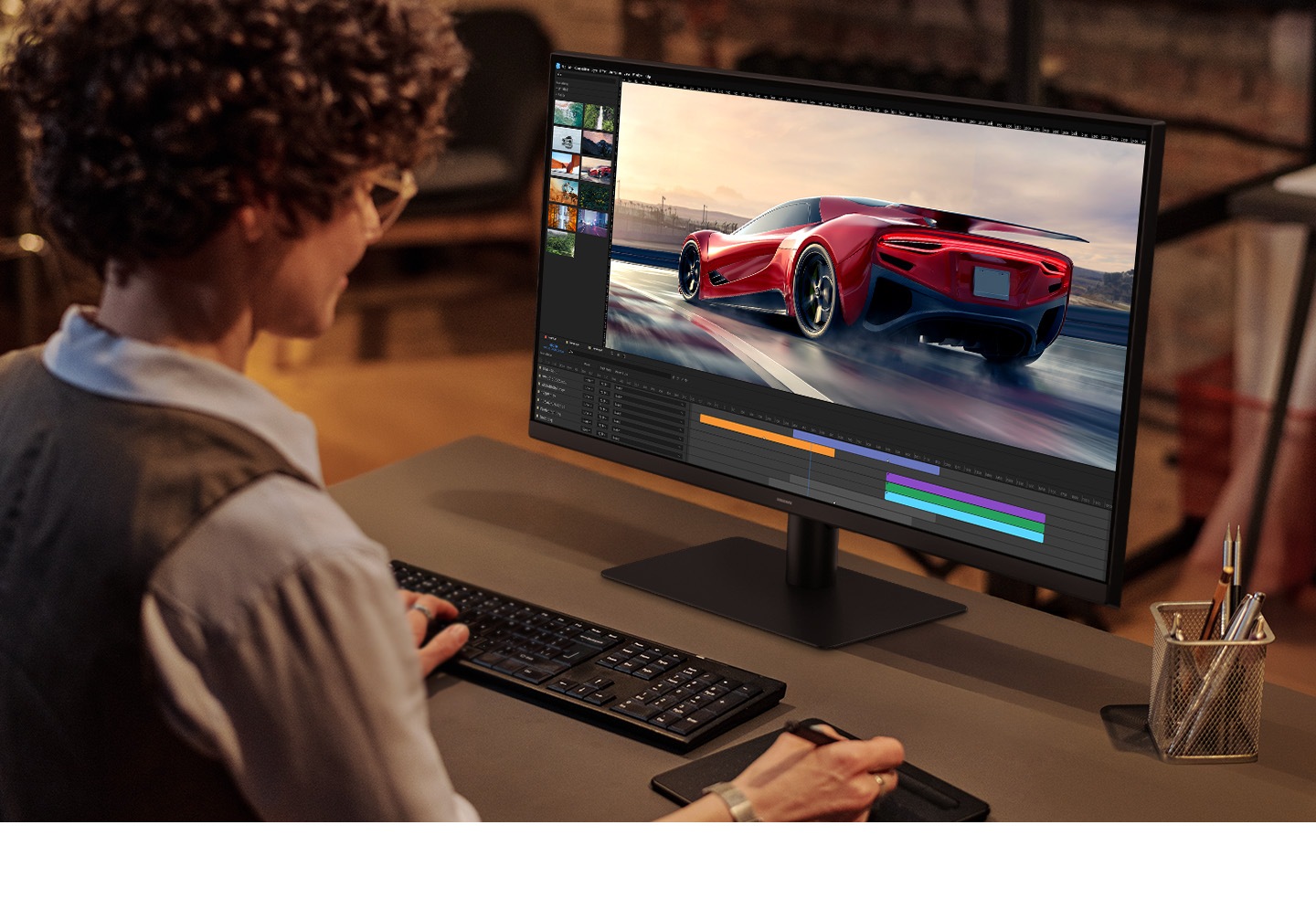 A curly-haired man is editing a red car video with a keyboard and pen tablet while looking at the monitor.
