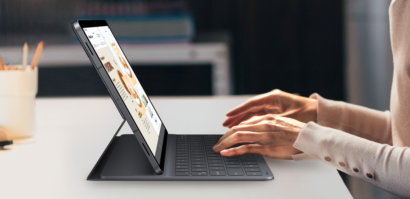 A person types on Galaxy Tab S11 using Book Cover Keyboard Slim. The screen displays Drawing Assist and Samsung Notes open side by side. The keyboard's sleek fit complements the tablet's design, highlighting a clean, professional setup for creative multitasking.