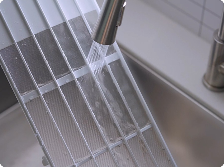 Shows the filter located at the top of the indoor unit being cleaned with water.