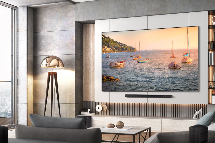 A 98 inch QLED TV hangs on the wall, showcasing a picturesque view of numerous boats sailing on the sea. Below the TV, a soundbar is installed.