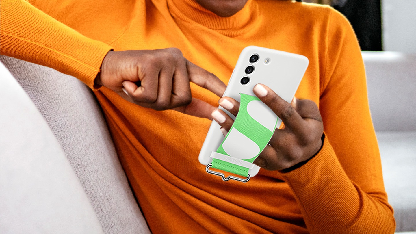  Una persona in possesso di Galaxy S21 FE 5G con la cover in silicone con cinturino installata. La mano sinistra della persona sta usando la cinghia sul retro della custodia per tenere il telefono.