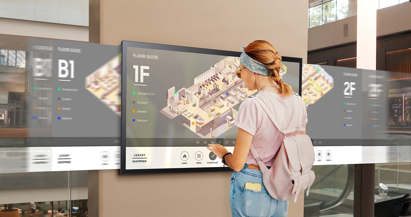 A woman touching the QMR-T. Floor guide maps are displayed next to the device.