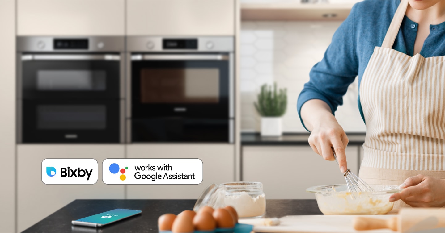 Shows a person baking while controlling the oven with their voice using a smartphone app, such as Bixby and Google Assistant.