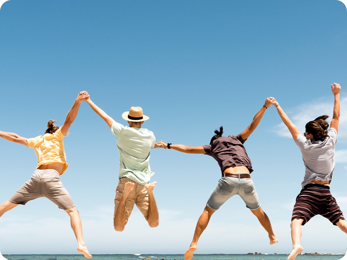 1. Photo taken with Wide-angle Camera showing four men holding hands and jumping on the beach in the daytime.