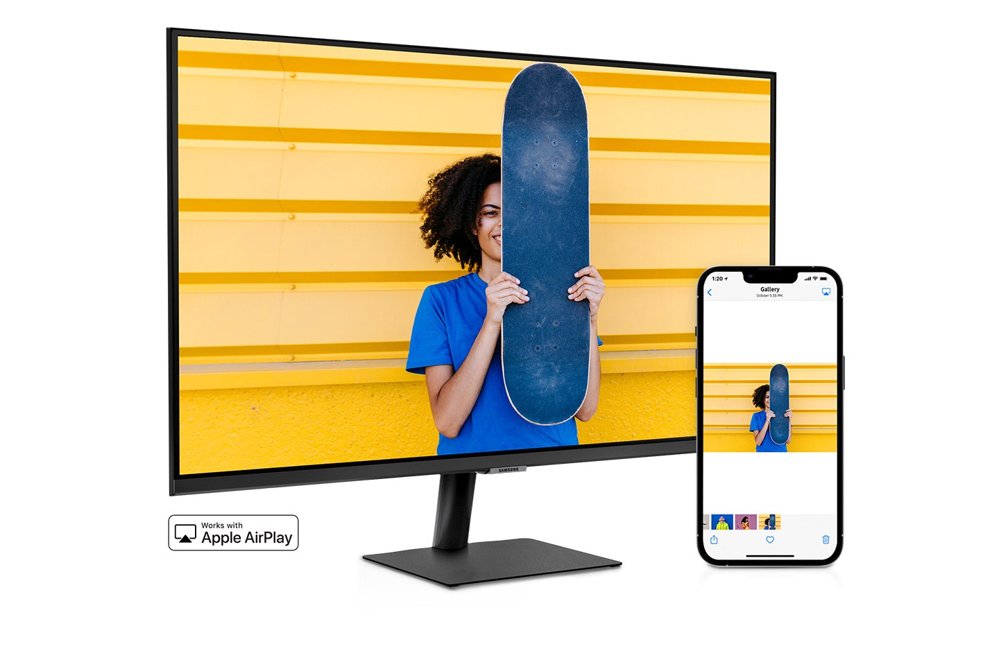 Un smartphone si un monitor stau unul langa altul.  Smartphone-ul arata o femeie care pozeaza cu un skateboard.  Aceeasi femeie cu skateboard este afisata pe monitor.  Aplicatia de galerie a smartphone-ului trece prin diferite fotografii care sunt afisate si pe ecranul monitorului.