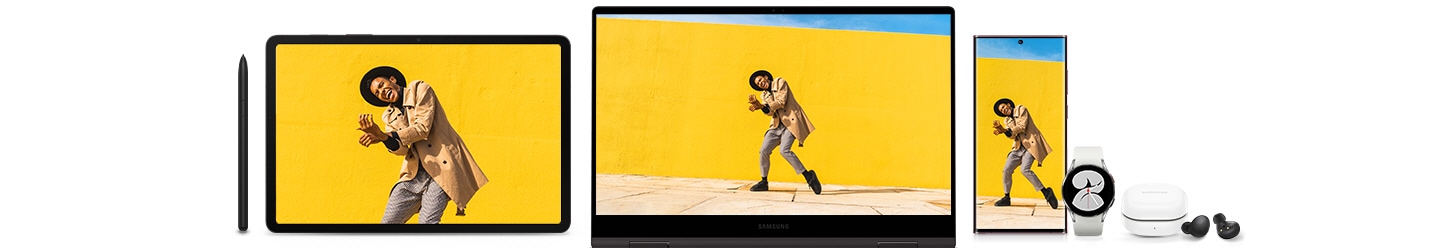 From left to right, there is an S Pen, a Galaxy Tab S8, a Galaxy Book2 360, a Galaxy S22 Ultra, a white Galaxy Watch4, a white Galaxy Buds2 case, and a pair of black Galaxy Buds next to it on the floor. On the screens of tablet, PC, and smartphone, is a man dancing in front of a yellow wall.
