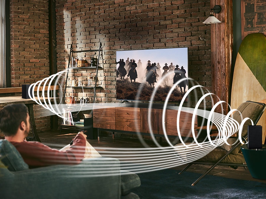 Un uomo ama i contenuti di corse sulla sua TV. Il kit di altoparlanti posteriori wireless Samsung e la soundbar creano un suono surround coinvolgente. Viene visualizzato il pulsante di commutazione.