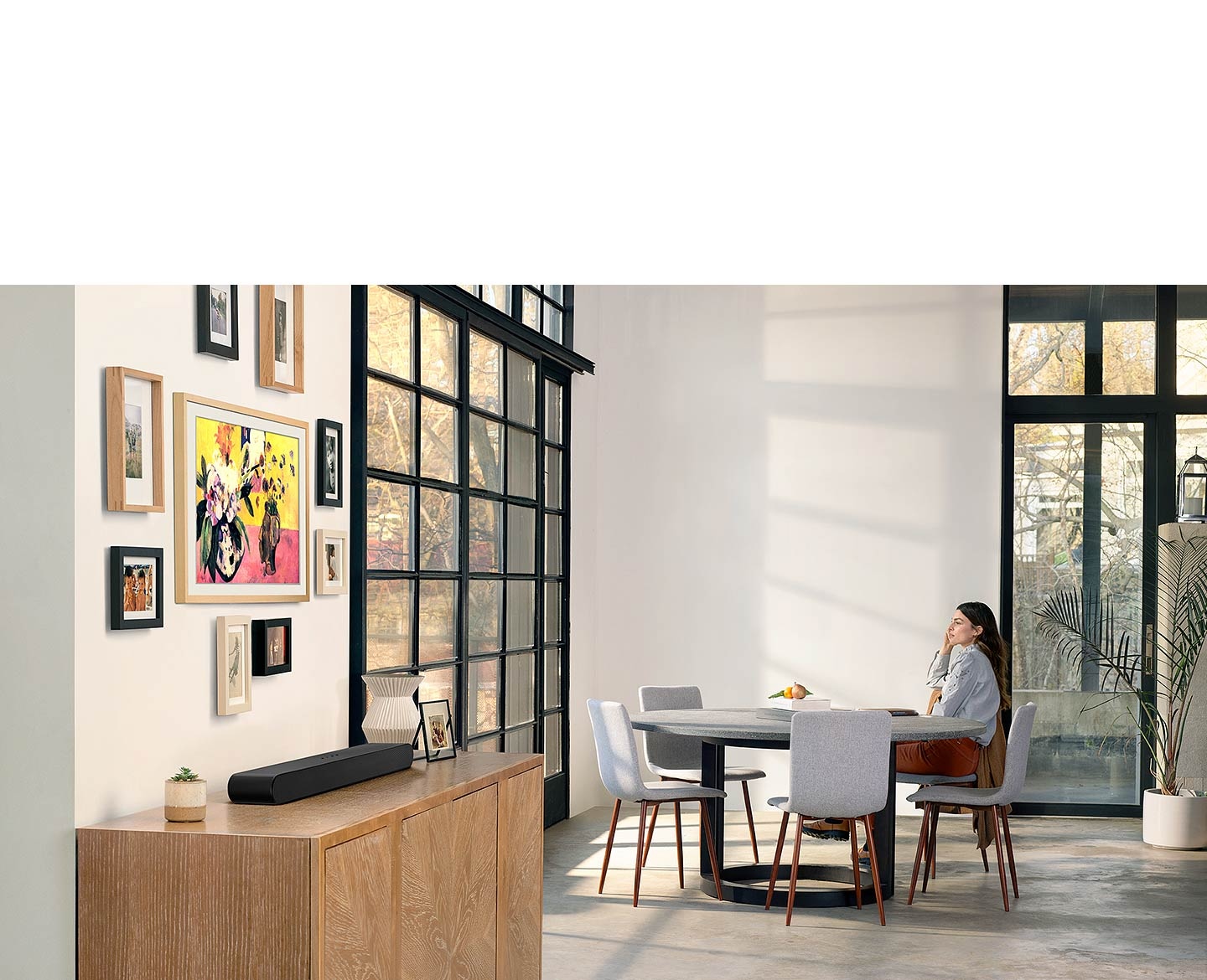  Il design all-in-one della soundbar S60B si fonde elegantemente con gli interni del soggiorno mentre una donna si siede al tavolo e guarda fuori dalla finestra.