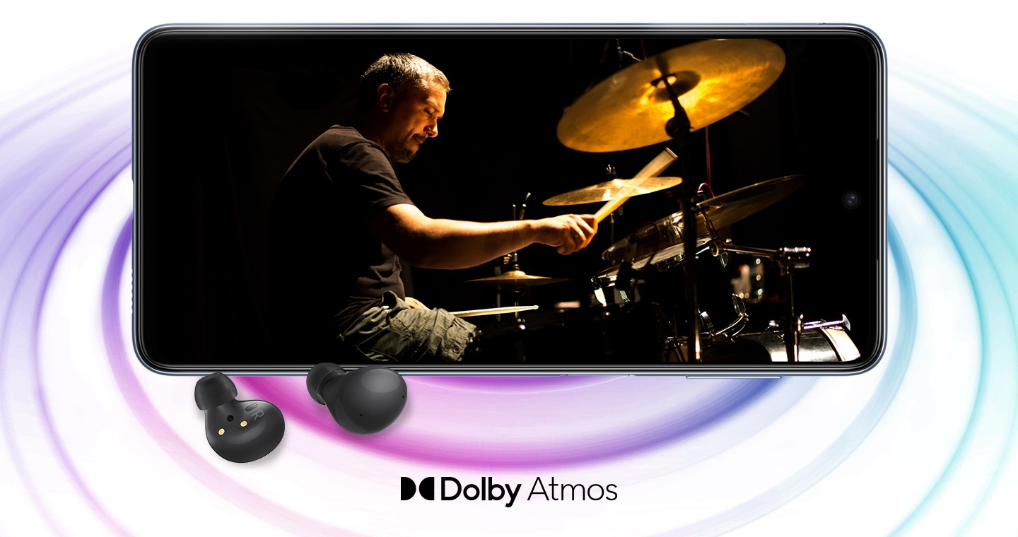 Galaxy M53 5G in landscape mode and an image with a man playing drums in the black background onscreen. A pair of black Galaxy Buds2 are placed in front of the device. The Dolby Atmos logo is shown below.