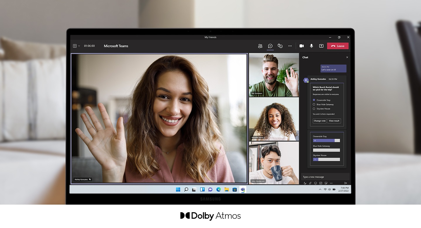 Galaxy Book2 обращен вперед, на экране происходит видеозвонок. Слева, занимая большую часть экрана, женщина улыбается и машет рукой. Справа от нее — трое других участников, двое мужчин и женщина. Справа находится чат. Под экраном ПК находится логотип Dolby Atmos.