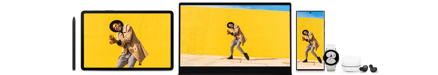 Слева направо на полу лежат S Pen, Galaxy Tab S8, Galaxy Book2, Galaxy S22 Ultra, белый Galaxy Watch4, белый чехол Galaxy Buds2 и пара черных Galaxy Buds рядом с ним. На экранах планшета, ПК и смартфона изображен мужчина, танцующий перед желтой стеной.