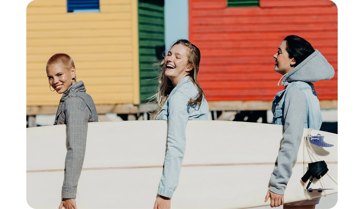  Tre ragazze sorridenti portano una tavola da surf. 