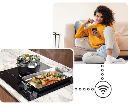 Due pentole con cibo delizioso stanno bollendo sul piano cottura e una donna sta monitorando lo stato del piano cottura da remoto vicino al divano tramite l'app SmartThings sul suo smartphone.