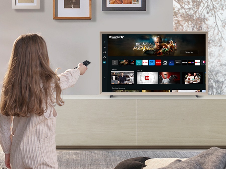 A girl is pointing the remote towards The Frame, which shows the Smart Hub home screen.