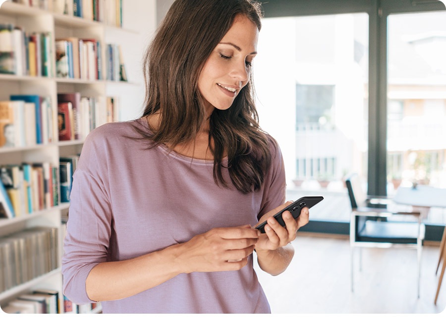 A smiling woman checks her phone. Onscreen is the SmartThings app with the status of a Less Microfiber™ Filter. A SmartThings app notification comes up on her phone’s home screen informing her that it’s time to clean the Less Microfiber™ Filter.