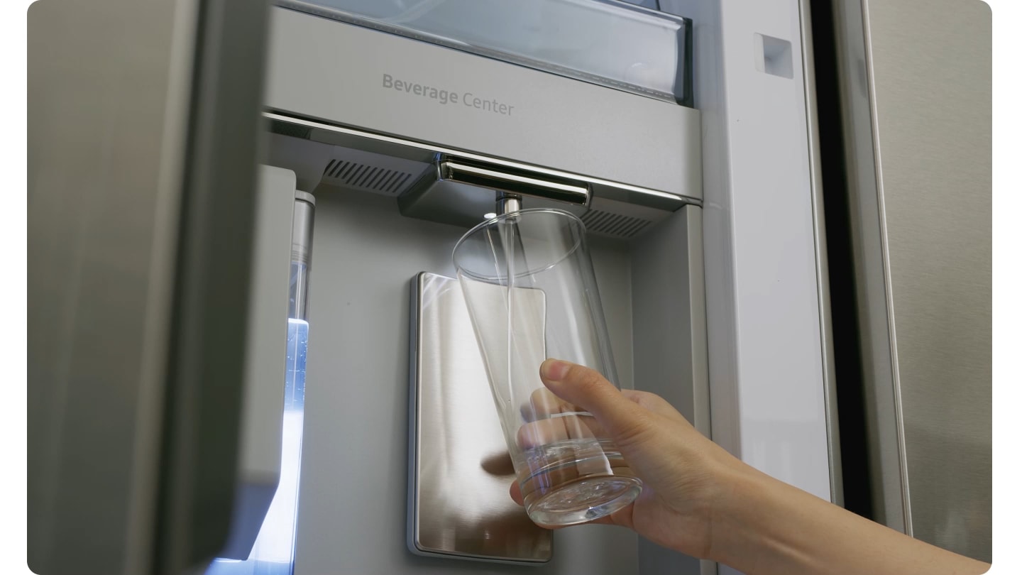 A close-up of a water pitcher with sliced limes being filled by the refrigerator's water dispenser transitions to a hand holding a glass being filled by the dispenser. The nozzle of the dispenser can be easily removed for cleaning.