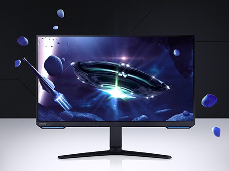 On a monitor screen shows two spaceships blasting through space surrounded by asteroids. The ship on the left is long and cylindrical and is traveling off-screen towards a shining, unknown planet. The second ship is saucer shaped and projects a bright light. Asteroids float off the gaming monitor's screen and surrounds the setting to recreate the display's immersive feeling.