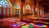 Light is shining through various color-stained windows and reflecting on the floor of inside structure. 