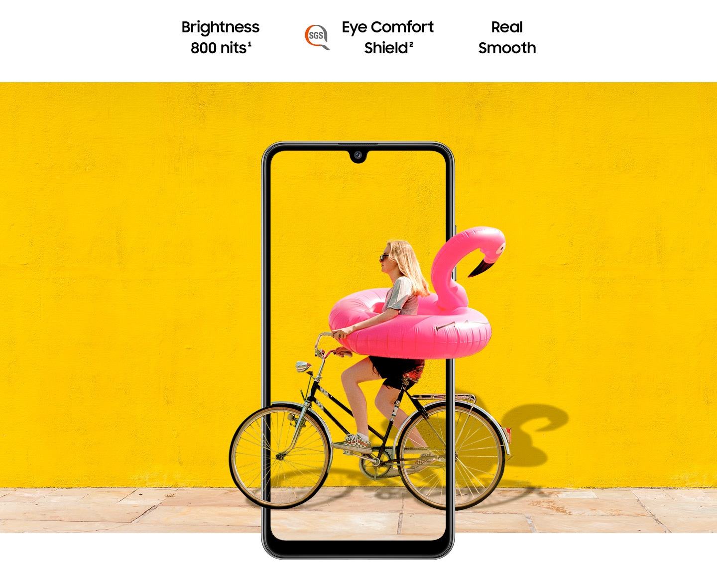 A woman on bike behind Galaxy A32. The picture goes the phone display's edges to represent its immersive view. Text says Brightness 800 nits, Eye Comfort Shield, with the SGS logo and Real Smooth.