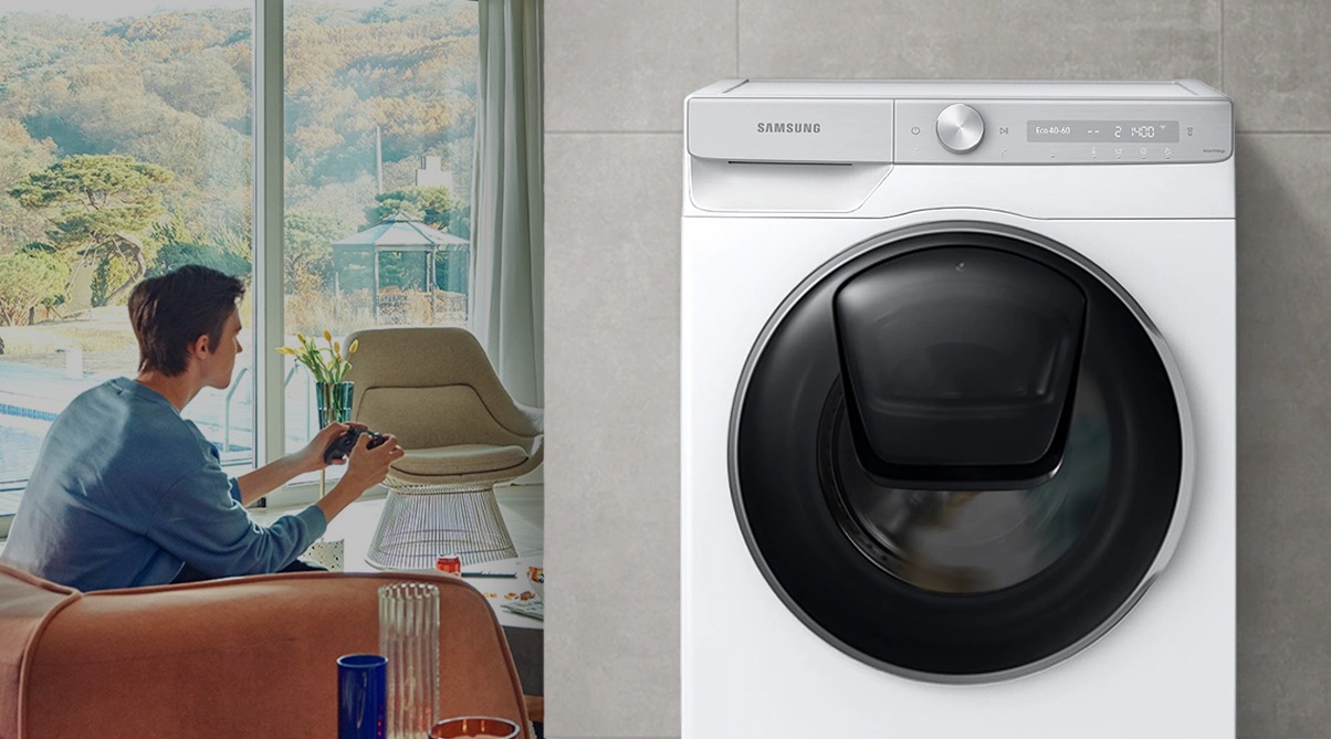 The boy reads the book during the day in the living room, while the washer runs silently next to him.