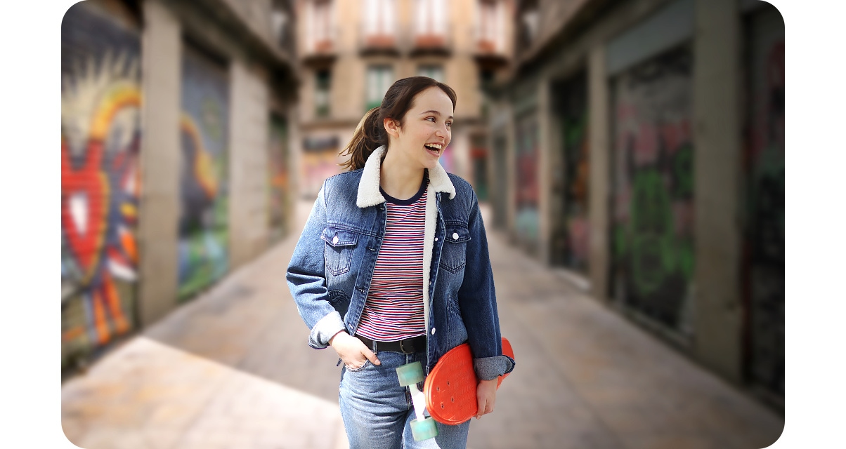 1. A woman is standing in front of an alleyway painted with colorful graffiti. However, with the Portrait On icon above activated, the background is blurred and the shot highlights the woman.