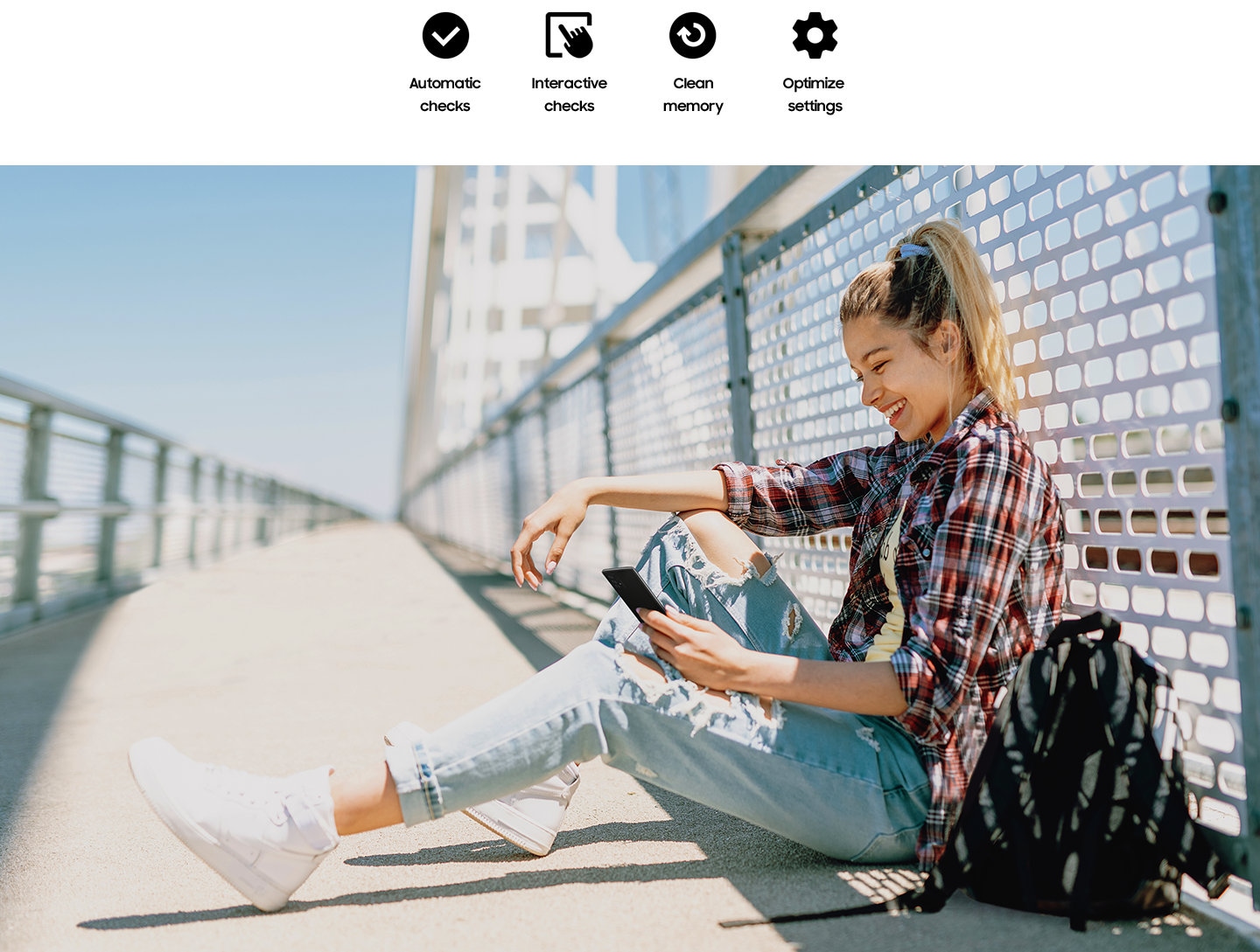 A woman is sitting down in the shade on a sunny day, on a bridge pathway with her back to the fence. She is looking at her Galaxy device and smiling. Text saying Automatic checks, Interactive checks, Clean memory and Optimize settings.