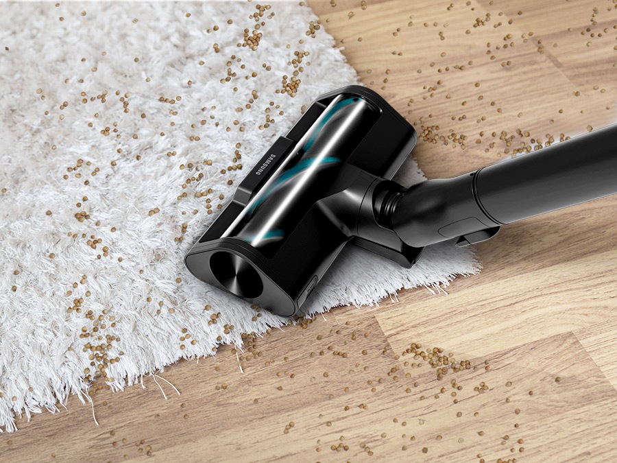 Крупный план активной двойной щетки, которая автоматически распознает и убирает мелкую пыль и мусор, разбросанные по белым коврам с длинным ворсом и деревянным полам.