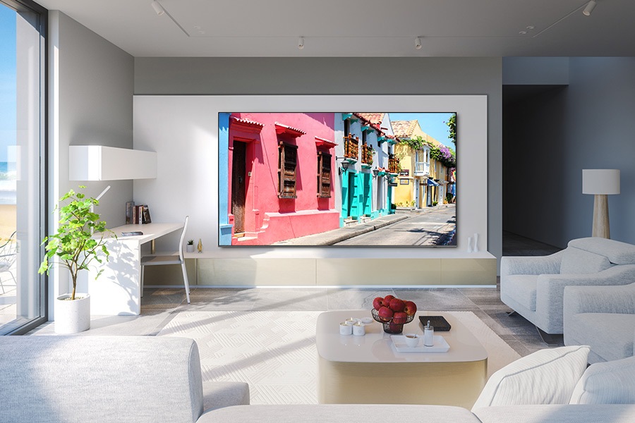 A 98 inch QLED TV hangs on the wall in a living room, displaying vibrant houses.