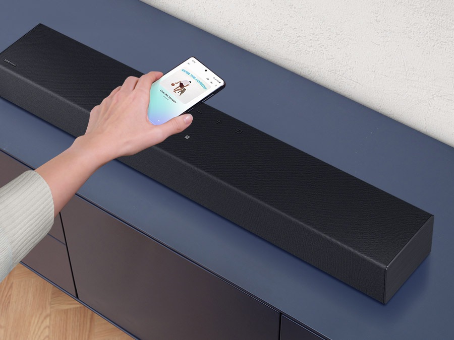 Una mano coloca un teléfono inteligente con la aplicación de música de Samsung en la barra de sonido y refleja fácilmente el audio de su móvil.