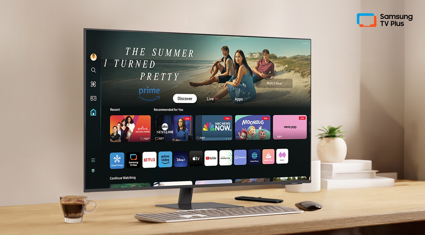 Hay un monitor en un escritorio y la interfaz del usuario local se muestra con aplicaciones OTT. En la parte superior derecha, hay un logotipo de Samsung TV Plus.