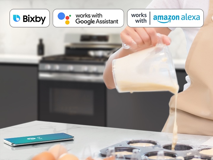 Shows a person baking while controlling the oven with their voice using a smartphone app, such as Bixby and Google Assistant.