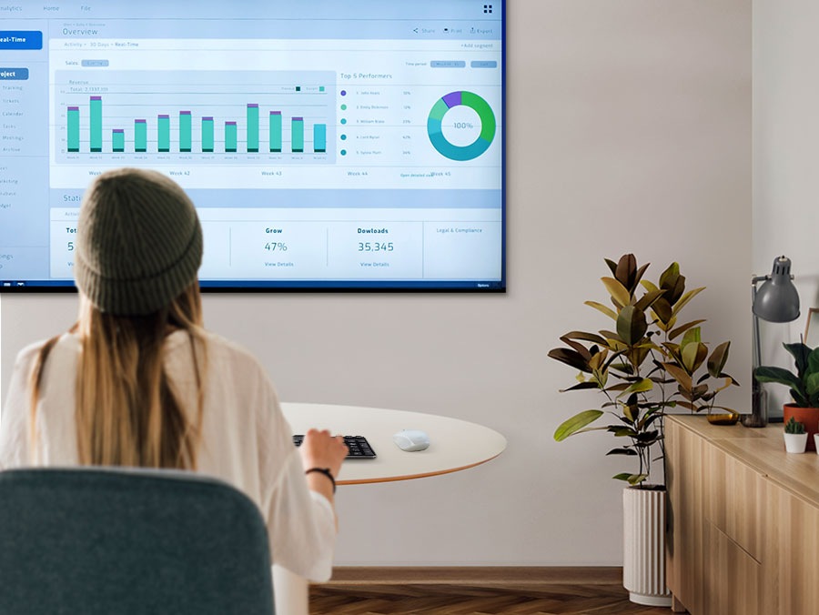 A woman is working from home in her living room and typing on a keyboard that's connected to a samsung smart TV.