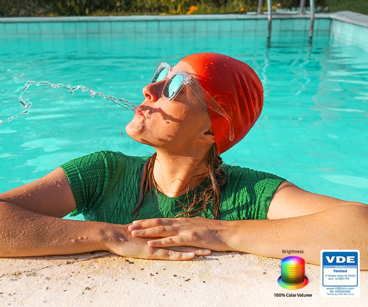 A woman is spitting out water in the pool. All the colors in the image become vivid as the brightness level increases. VDE tested logo is on display.