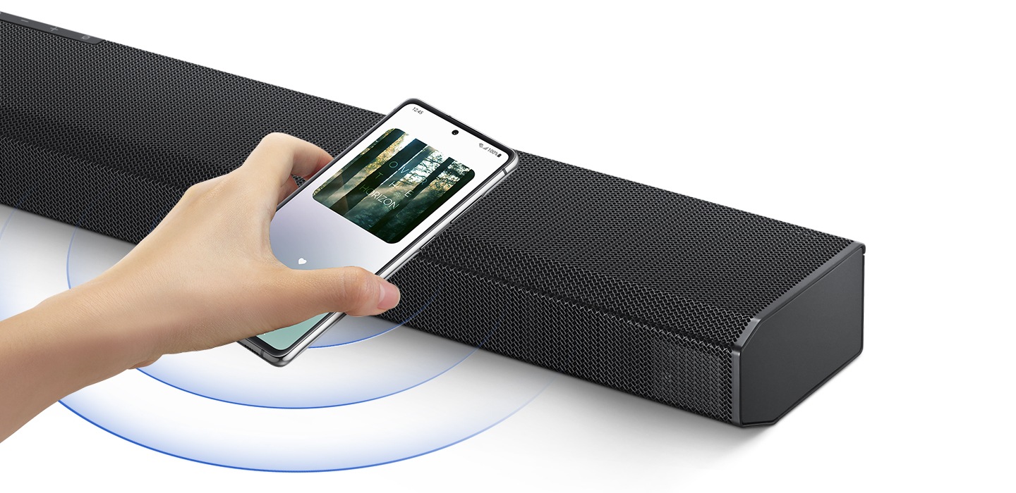 A hand taps a smartphone with the Samsung music app on-screen on the soundbar and the soundbar instantly plays music, showing how easy it is to switch from smartphone to soundbar.