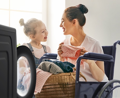 A woman with a disability is happily doing laundry with her daughter.