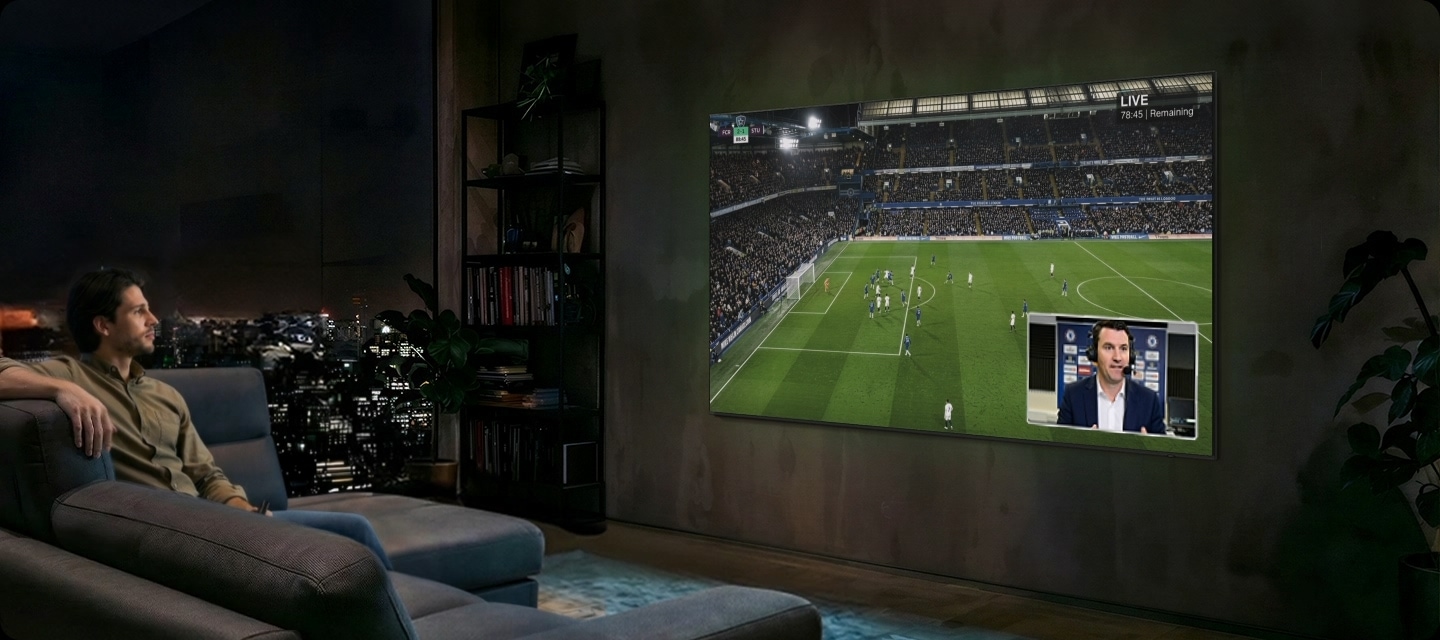 Man watches football on Samsung TV at night. Soundwaves emanate from TV's side and front. He speaks into remote control ‘Bixby, AI Football Mode ON’. AI Football Mode turns on, soundwaves show balanced crowd and commentator sound, and the field looks more crisp and vibrant than when it's off.