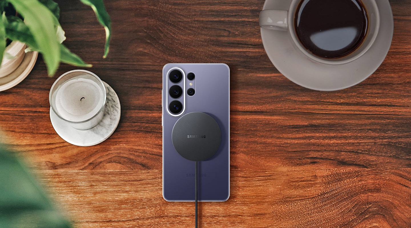 Top-down view of a Galaxy S26 Ultra in Cobalt Violet on a wooden surface in the Clear Magnet Case with the Magnet Wireless Charger aligned on the back, highlighting effortless charging.