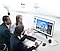 There are IPS Panel and Wide Viewing Angle icons. Three people are sitting around the monitor with the monitor in the middle, looking at the monitor and having a conversation.