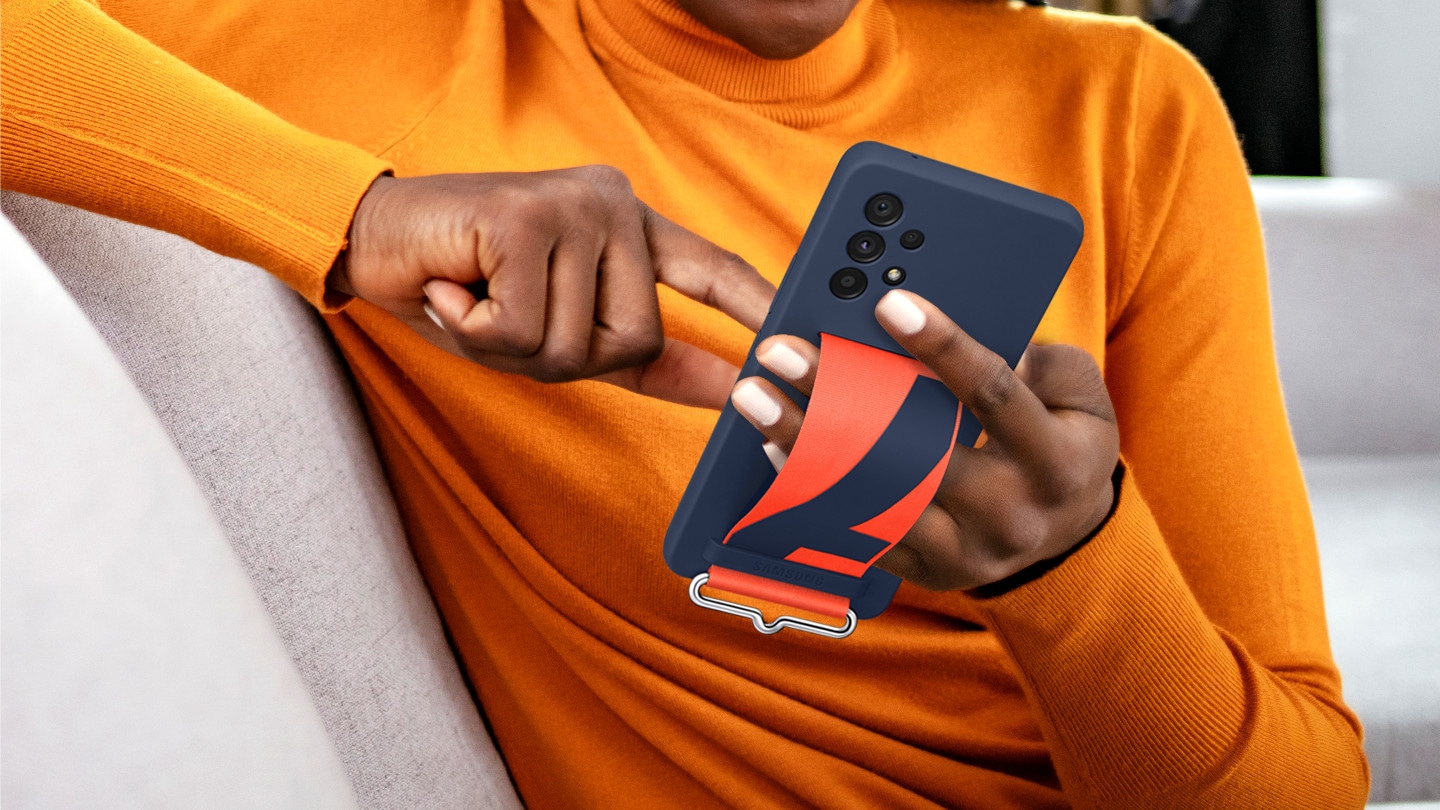 A man is in a comfortable position while using his Galaxy A53 wearing a Silicone Cover with Strap by holding onto it comfortably with one hand using the strap.