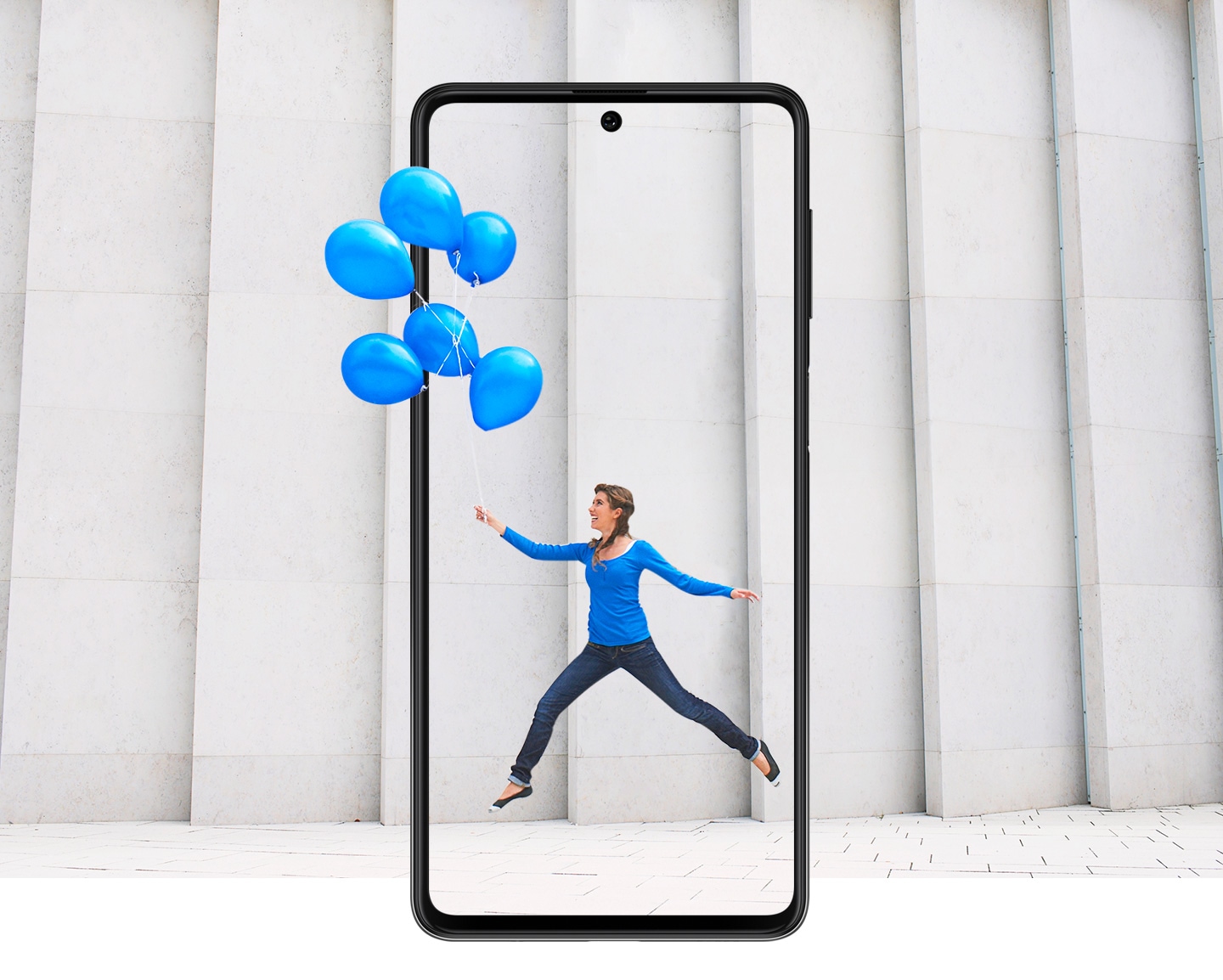 Une fille vêtue de vêtements bleus tient des ballons bleus, sautant en mouvement capturé dans l'écran Galaxy M62 infinity-O.