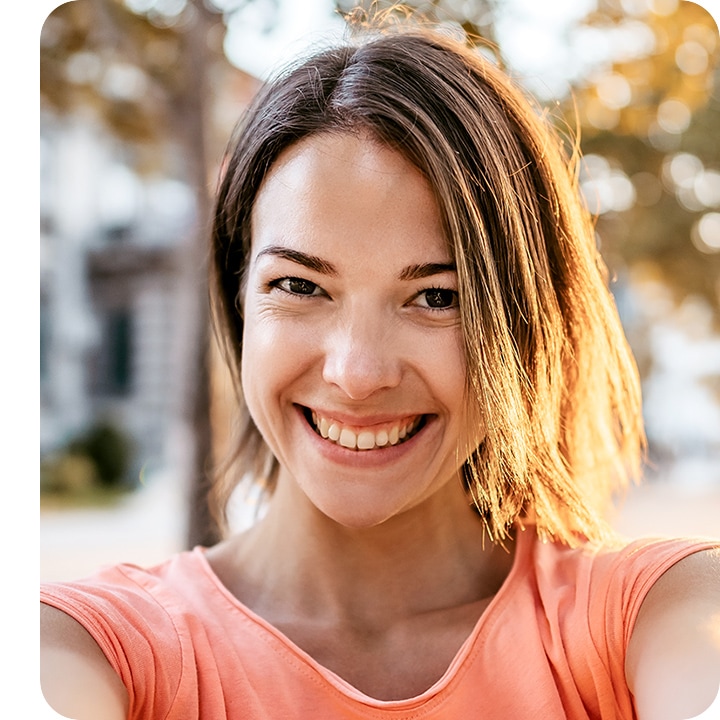 A woman looking into the camera, taking a selfie. The background is subtly blurred out with the bokeh effect.