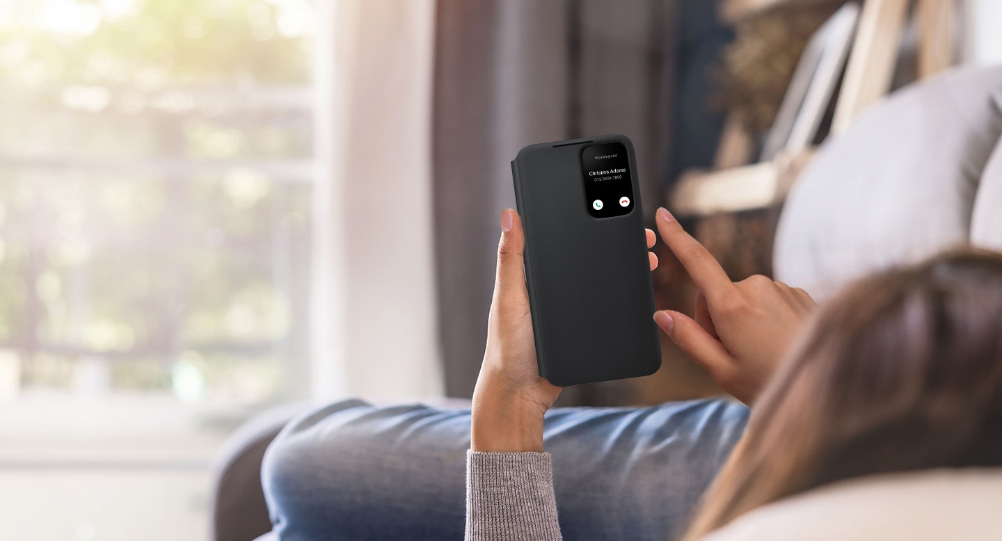 A person lying down, holding Galaxy S22 with the Smart Clear View Cover installed and the front cover closed. A call notification is seen in the cover window.