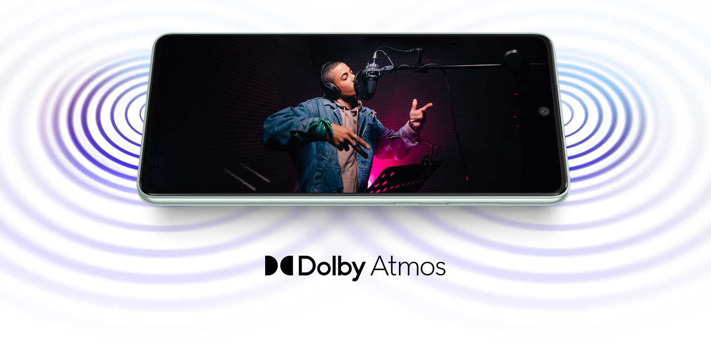 Galaxy A73 5G is laid horizontally and shows sound coming from both ends of the device. On screen, a male artist wearing headphones is singing into a studio microphone in a recording session. The Dolby Atmos logo is shown below.