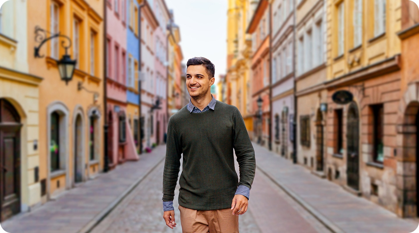 A man is smiling as he walks down a cobblestone paved street. The background, which has many colorful buildings, is blurred slightly to help make him stand out in the picture.