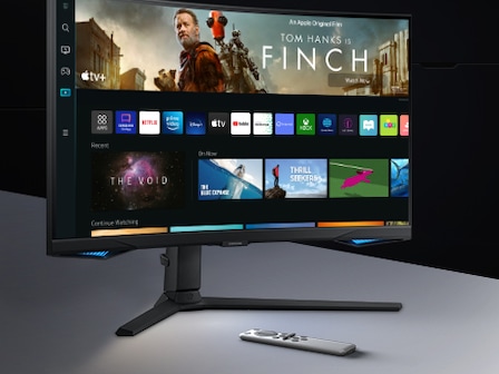The monitor screen shows a variety of content apps and individual content choices in a card format. A remote controller rests next to the monitor.