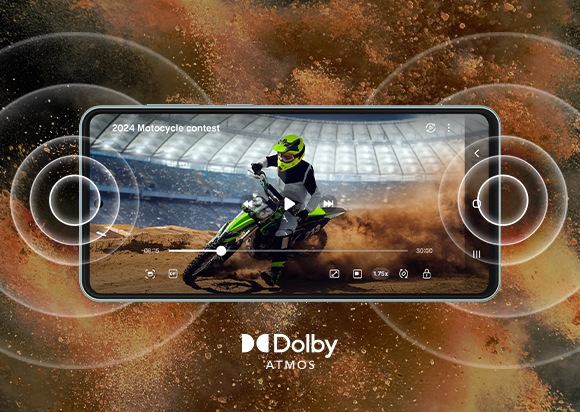 A Galaxy M55 5G device, shown horizontally, shows a video of a dirt biker on a neon green dirt bike. The title of the video reads, '2024 Motorcycle contest' and below the device is the Dolby Atmos logo. The background behind the device is filled with dirt being sprayed up into the air while the device has rings of concentric circles extending from both ends of the device.