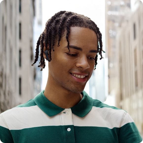 A man wearing Black Galaxy Buds3 FE outdoors, featuring a cityscape in the background.