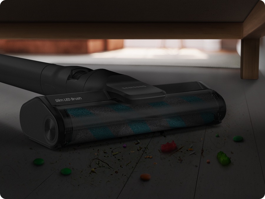 A Jet 95 with a slim LED Brush reaches underneath a sofa to vacuum dirt. LED lighting is off.