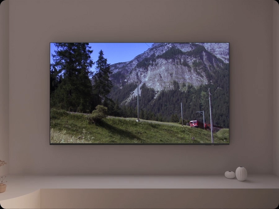A TV depicts a scene of a train passing by a scenic outdoor location. As it does, sound waves appear near where the train touches the tracks, indicating the noise within the scene.