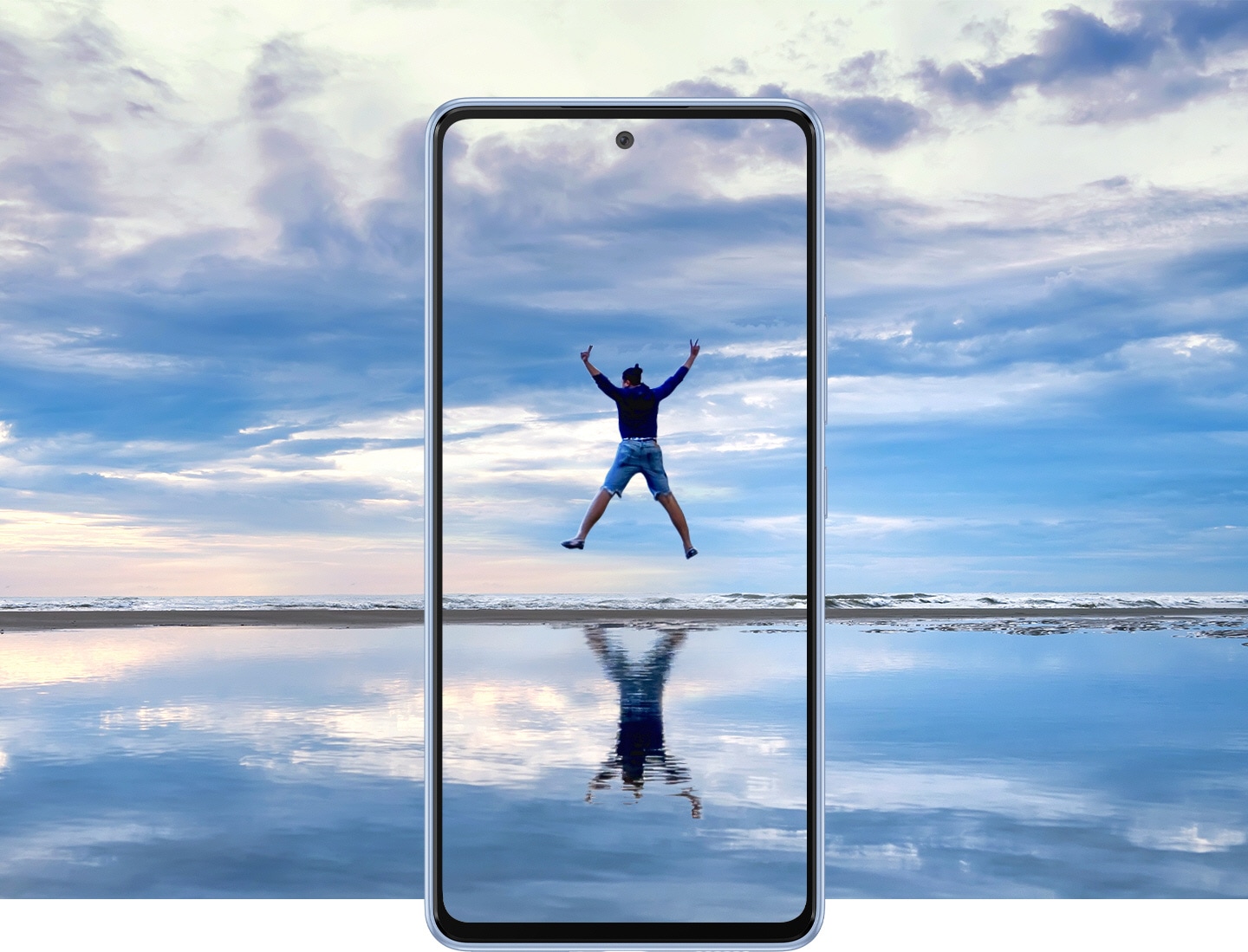 Galaxy A53 5G seen from the front against a beautiful landscape that overlaps onto the screen. It shows an expansive sky over water that reflects it with a thin horizon dissecting near the middle. In the center of the screen, a man is jumping in the air with all four limps outstretched and his reflection is shown on the water.